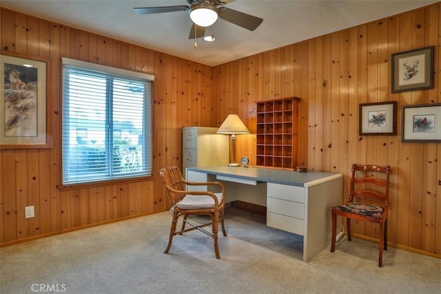 office featuring baseboards, light colored carpet, wood walls, and a ceiling fan