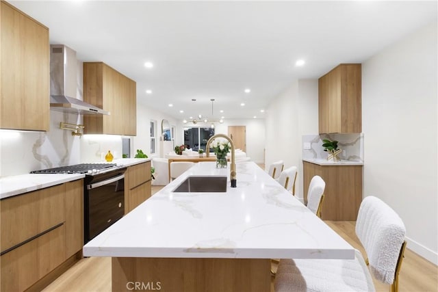 kitchen with a large island with sink, a sink, gas range, wall chimney range hood, and modern cabinets