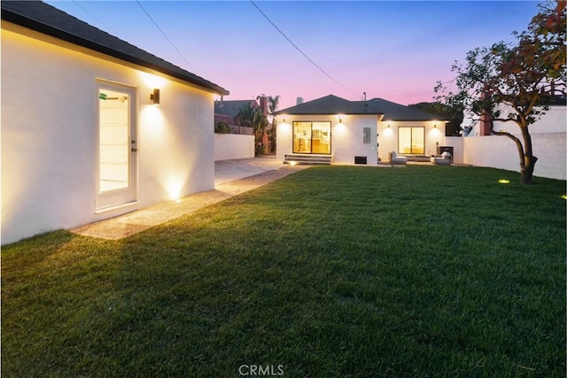 rear view of property with stucco siding, a patio, a lawn, and fence