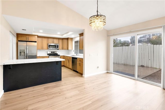 kitchen with light wood finished floors, stainless steel appliances, decorative backsplash, a raised ceiling, and decorative light fixtures