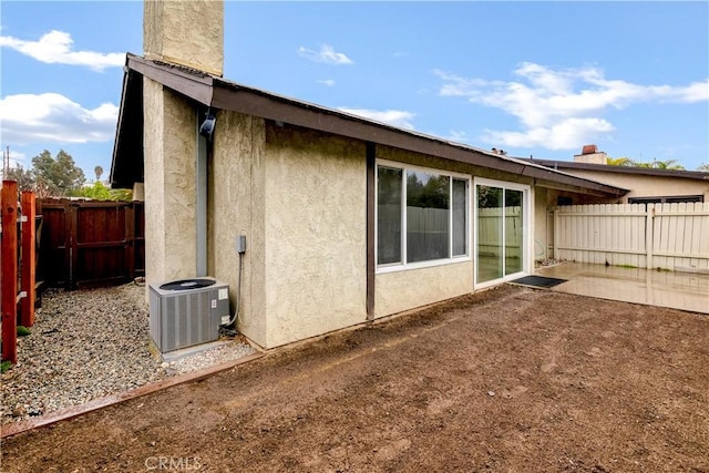 view of home's exterior featuring a fenced backyard, stucco siding, a chimney, and central AC