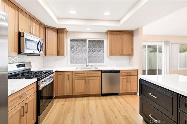 kitchen with light wood finished floors, light countertops, stainless steel appliances, a raised ceiling, and a sink