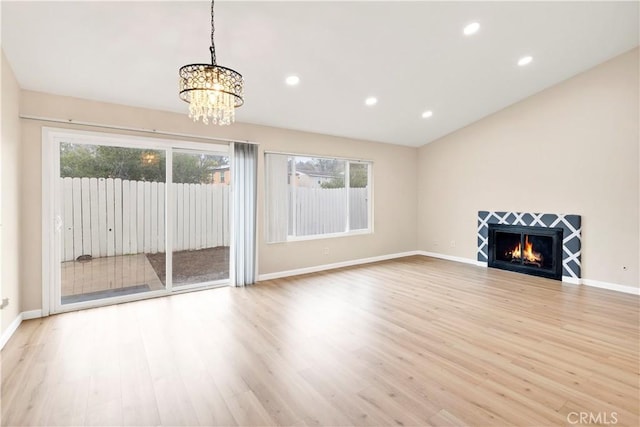 unfurnished living room featuring wood finished floors, baseboards, an inviting chandelier, recessed lighting, and a tiled fireplace