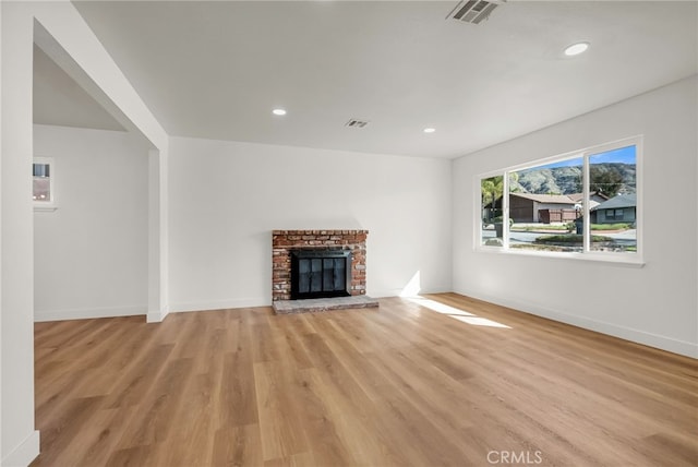 unfurnished living room with visible vents, baseboards, light wood-style floors, and a brick fireplace