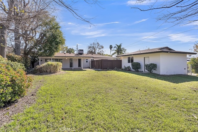 back of property with stucco siding, a lawn, and fence