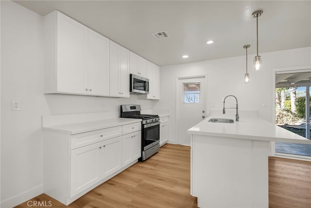 kitchen with visible vents, a peninsula, a sink, stainless steel appliances, and light wood-type flooring