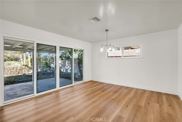 spare room featuring light wood-type flooring, visible vents, baseboards, and a notable chandelier