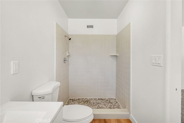 bathroom featuring vanity, toilet, visible vents, and tiled shower