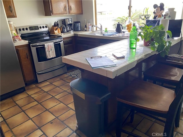 kitchen with light tile patterned floors, a peninsula, appliances with stainless steel finishes, and tile counters