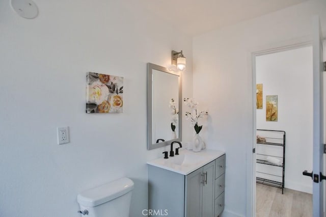 bathroom with toilet, vanity, baseboards, and wood finished floors