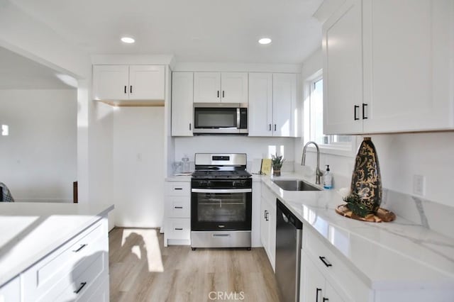 kitchen with a sink, recessed lighting, stainless steel appliances, white cabinets, and light wood finished floors