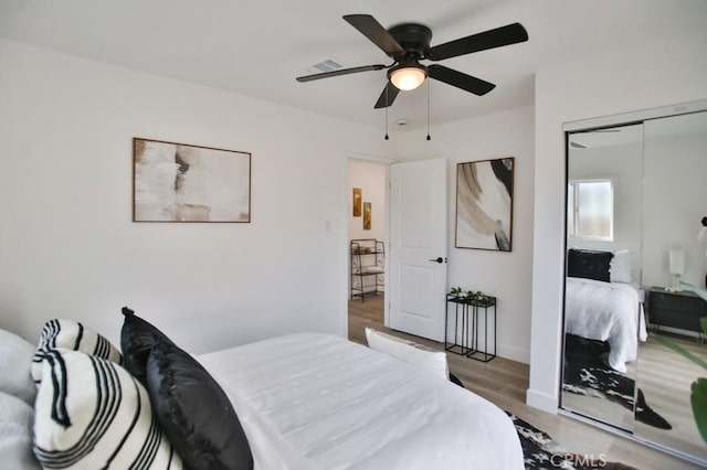 bedroom with a ceiling fan, wood finished floors, visible vents, and a closet