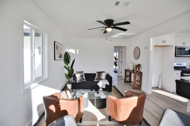 living room with visible vents, light wood-style floors, and ceiling fan