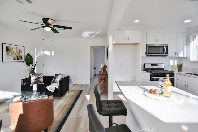 kitchen with light wood finished floors, ceiling fan, light countertops, appliances with stainless steel finishes, and white cabinetry