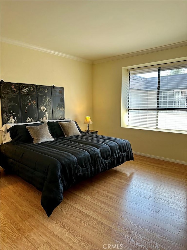 bedroom featuring baseboards, wood finished floors, and crown molding