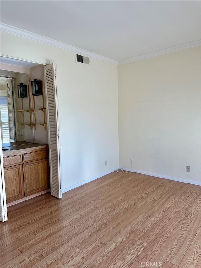 empty room with visible vents, baseboards, light wood-style floors, and crown molding