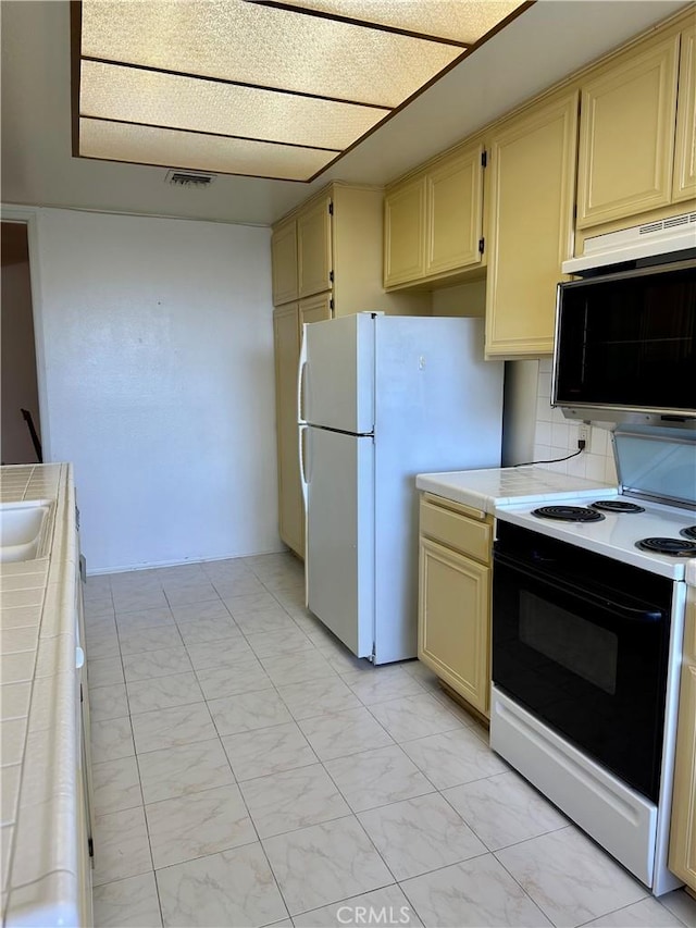 kitchen featuring cream cabinetry, tile countertops, white appliances, and visible vents