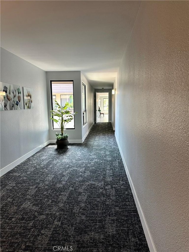 hallway featuring dark carpet, baseboards, and a textured wall