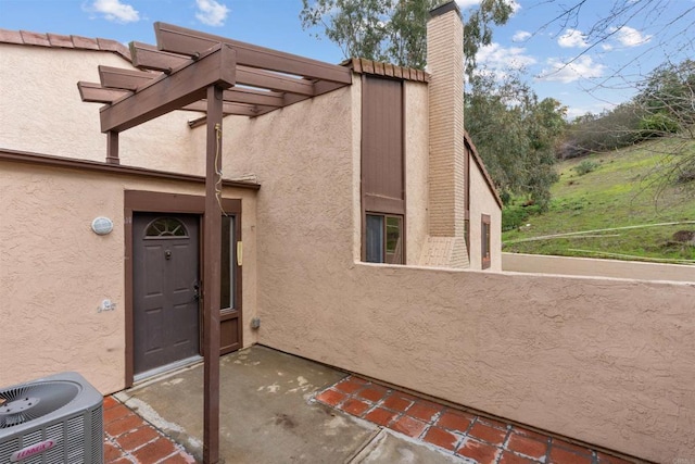 doorway to property featuring central AC unit, a chimney, and stucco siding