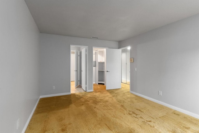 unfurnished bedroom with baseboards, visible vents, a closet, light carpet, and a walk in closet