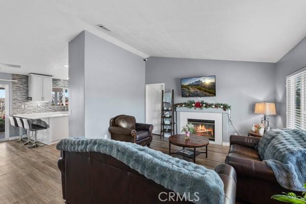 living area featuring visible vents, lofted ceiling, a warm lit fireplace, and wood finished floors