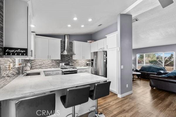 kitchen featuring light stone counters, a peninsula, a sink, appliances with stainless steel finishes, and wall chimney exhaust hood