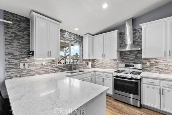 kitchen featuring gas stove, white cabinetry, a sink, and wall chimney range hood