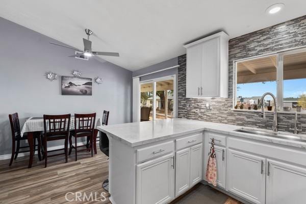 kitchen with a ceiling fan, a sink, white cabinetry, a peninsula, and light countertops