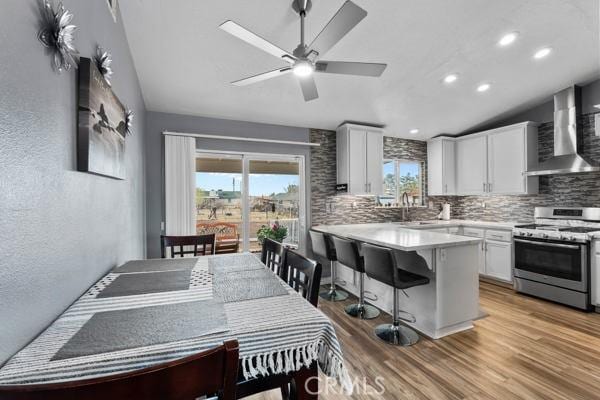 kitchen with plenty of natural light, white cabinetry, stainless steel gas range, and wall chimney exhaust hood