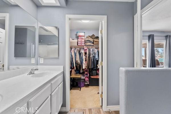 bathroom featuring double vanity, a spacious closet, wood finished floors, and a sink