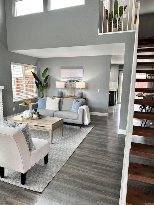 living area featuring stairway, baseboards, dark wood-style floors, and a towering ceiling