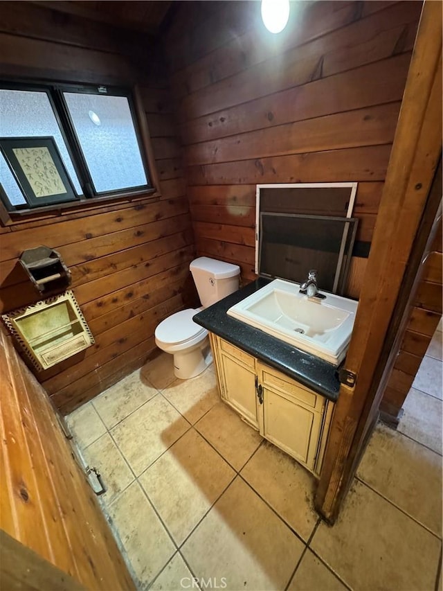 half bath with tile patterned floors, toilet, wood walls, and vanity