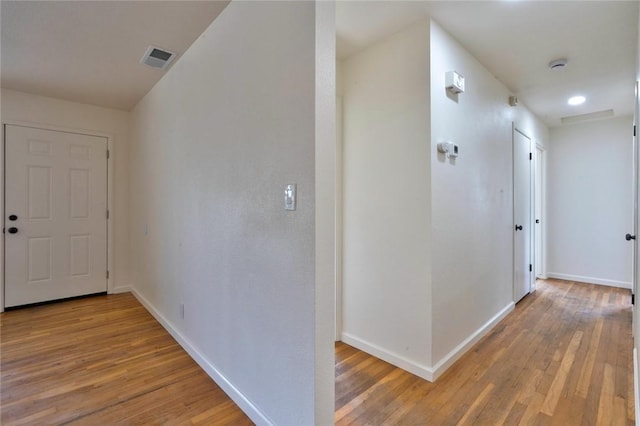 hall with light wood-style flooring, baseboards, and visible vents