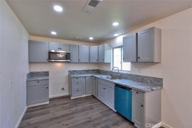 kitchen featuring stainless steel microwave, visible vents, dishwashing machine, wood finished floors, and a sink