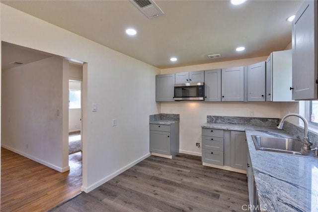 kitchen featuring visible vents, dark wood-type flooring, gray cabinets, a sink, and stainless steel microwave