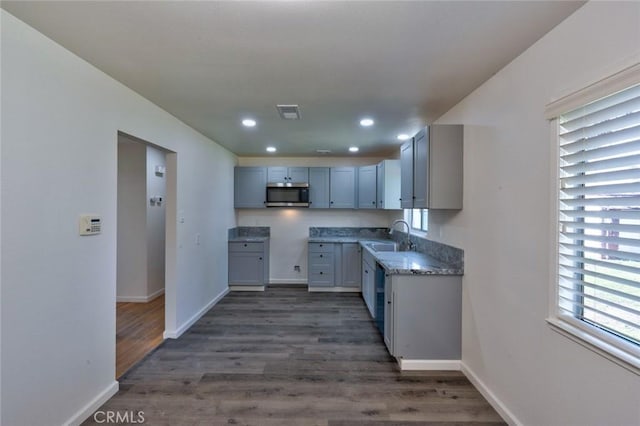 kitchen featuring stainless steel microwave, dark wood-type flooring, baseboards, and a sink