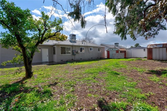 rear view of house featuring a shed, a lawn, an outdoor structure, and stucco siding