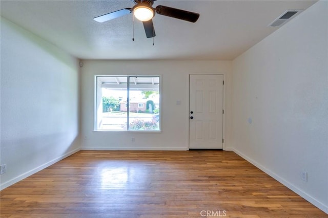 empty room with ceiling fan, visible vents, baseboards, and wood finished floors