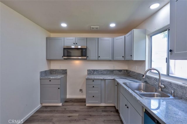 kitchen with visible vents, a sink, stainless steel microwave, dark wood-style floors, and baseboards