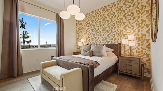 bedroom featuring wallpapered walls, wood finished floors, baseboards, and an accent wall