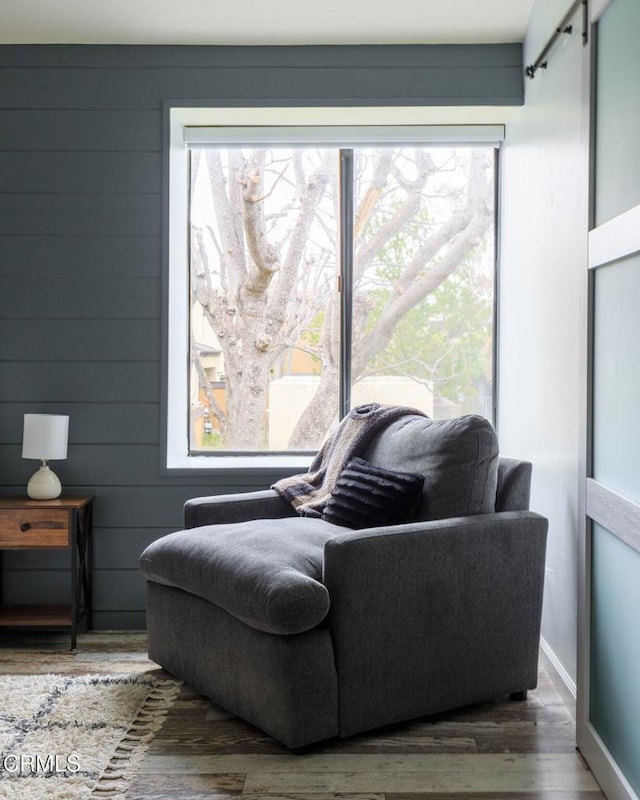 sitting room with a barn door, wood finished floors, baseboards, and wood walls