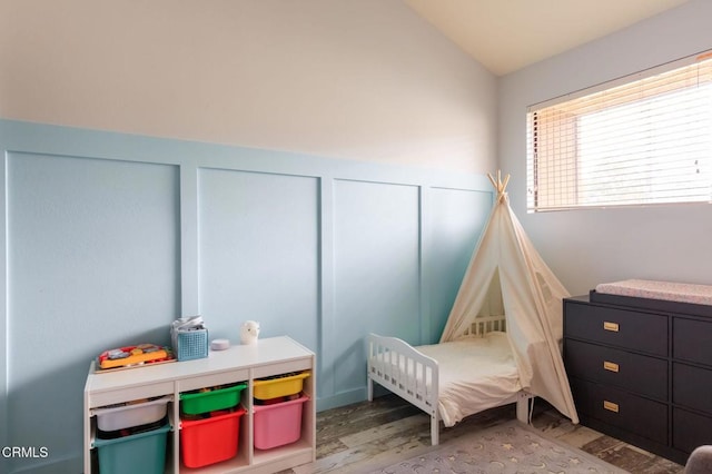 bedroom with a decorative wall, a wainscoted wall, wood finished floors, and vaulted ceiling