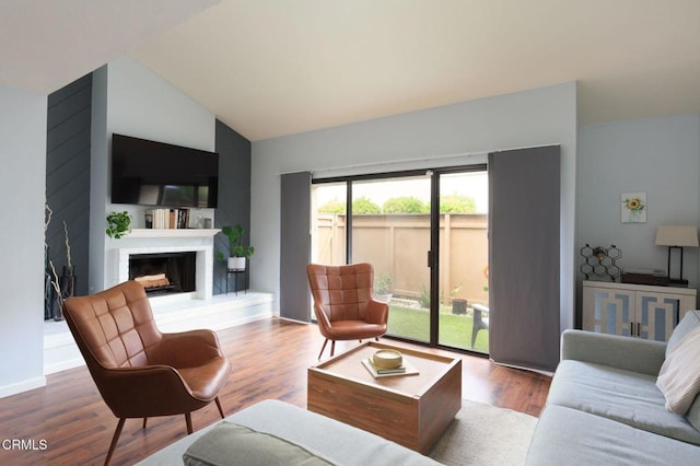 living area with a fireplace, wood finished floors, baseboards, and vaulted ceiling