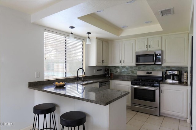 kitchen with visible vents, a tray ceiling, a peninsula, stainless steel appliances, and a sink