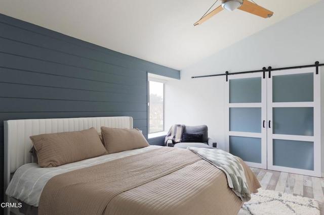 bedroom with a ceiling fan, a barn door, wood finished floors, and lofted ceiling