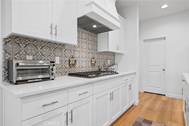 kitchen with premium range hood, light wood-type flooring, stainless steel gas cooktop, a toaster, and tasteful backsplash