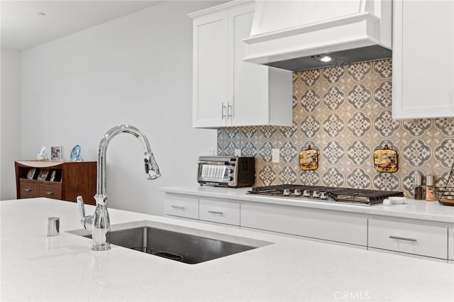 kitchen featuring premium range hood, a sink, stainless steel gas stovetop, a toaster, and decorative backsplash