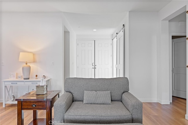 sitting room with light wood-style flooring, baseboards, and a barn door