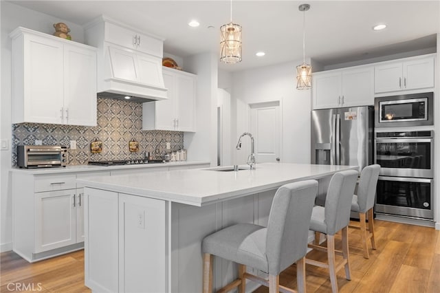 kitchen with light wood-type flooring, an island with sink, a sink, appliances with stainless steel finishes, and light countertops