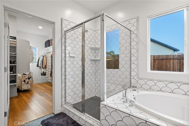 full bath with a spacious closet, a stall shower, a bath, and wood finished floors